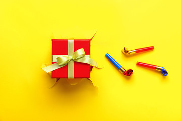 Beautiful gift with party whistles on color background