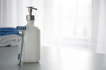 Bottle of cosmetics with razor on table