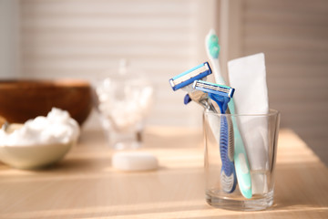 Glass with razors, tooth paste and brush on table in bathroom