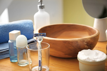 Razor with shaving foam and cosmetics on table in bathroom