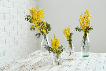 Glassware with beautiful mimosa flowers on white table in room - obrazy, fototapety, plakaty