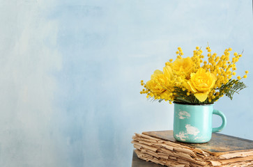Cup with beautiful yellow flowers and old book on color background