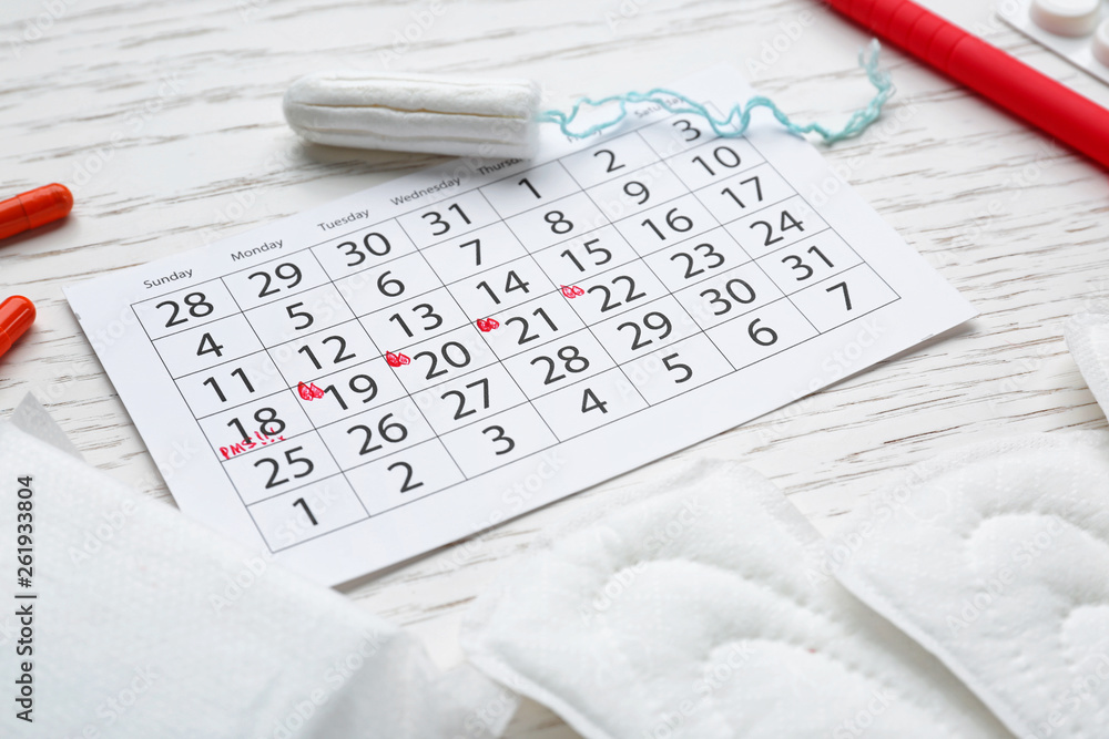 Wall mural Menstrual calendar with feminine products and pills on white table