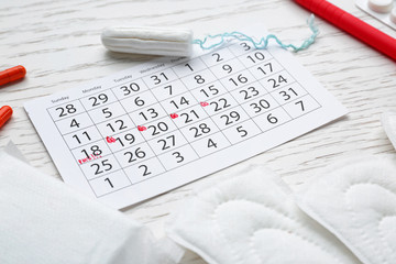 Menstrual calendar with feminine products and pills on white table