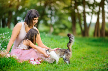 family is having fun. Mom and daughter play in the cat sitting on the grass in the park. people concept. Family enjoy time together