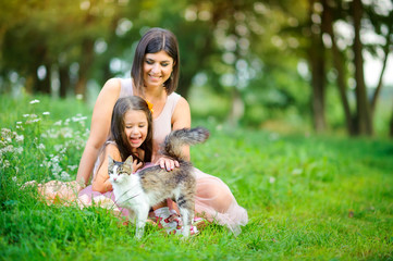 Obraz premium family is having fun. Mom and daughter play in the cat sitting on the grass in the park. people concept. Family enjoy time together