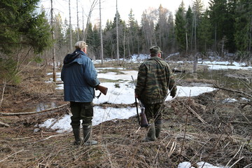 Hunting scene with group of hunters in camouflage walking in spring forest with dry leaves during...