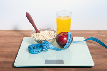 The concept of healthy diet, fitness and weight loss. Scales, measure tape, oatmeal, apple, a glass of juice on the table.