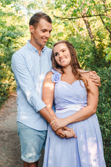 Fototapeta premium Couple in love smiling and hugging in trees tunnel. Man holding hands around woman. Tender and affectionate couple standing on nature background. Young beautiful couple. Happy couple in love