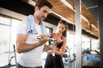 Rolgordijnen FIt happy woman personal trainer helping man in gym © NDABCREATIVITY