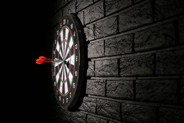 Dartboard with hit bullseye on dark brick wall