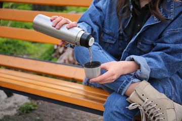 Woman drinking hot tea from thermos outdoors