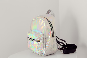 Stylish backpack from iridescent material on table near white wall