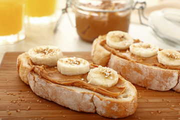 Bread with tasty peanut butter and banana on wooden board, closeup