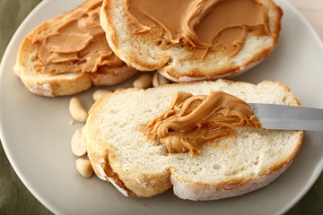 Bread with tasty peanut butter on plate, closeup