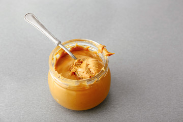 Tasty peanut butter in jar on grey table