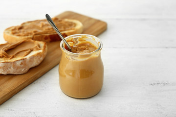 Tasty peanut butter in jar and fresh bread on white table