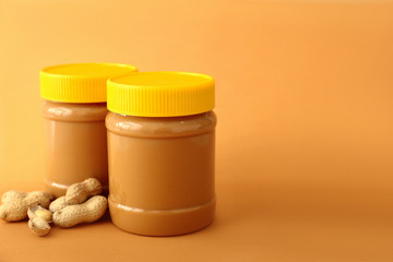 Tasty peanut butter in jars on color background