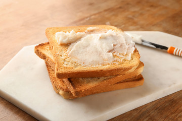 Board with coconut oil and tasty toasted bread on wooden table