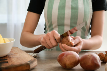 Woman peeling raw potato at table in kitchen