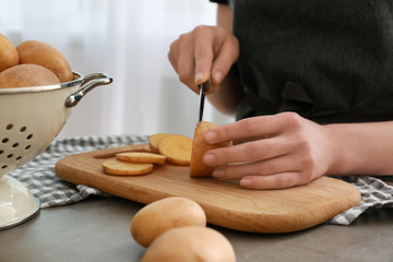 Woman cutting raw potato at table in kitchen