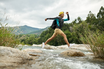 Traveler running through shallow rocky river on nature background