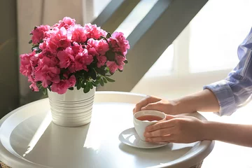 Crédence de cuisine en verre imprimé Azalée Femme buvant du thé à table avec une belle azalée en fleurs