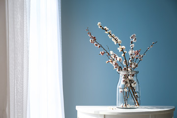 Vase with beautiful blossoming branches on table near window