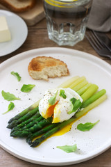 Breakfast consisting of poached egg and boiled asparagus with butter and lettuce on a wooden surface. Rustic style.