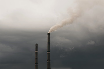 Industrial smoke emissions from chimneys on dark cloud sky background.