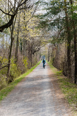 Fototapeta na wymiar sporty woman riding a bicycle along a dirt path through a beautiful spring time colorful forest