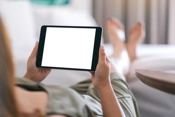 Mockup image of a woman holding and using tablet pc with blank screen horizontally while relaxing and lying on the bed