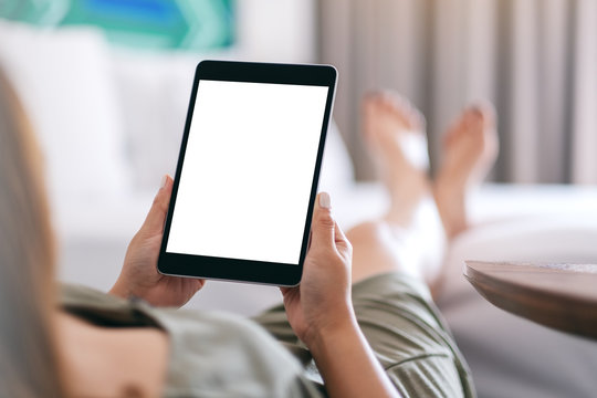 Mockup image of a woman holding and using tablet pc with blank screen while relaxing and lying on the bed