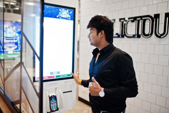 Indian man customer at store place orders and pay through self pay floor kiosk for fast food, payment terminal. He show thumb up.