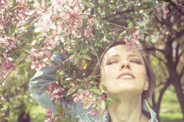 Young woman in spring park with blooming beautiful trees around