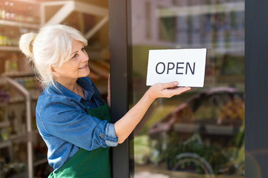 Senior Woman Holding Open Sign In Organic Produce Shop