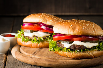 Close-up photo of home made hamburger with beer made of beef, onion, tomato, lettuce, cheese and spices. Fresh burger closeup on wooden rustic table with potato fries and chips.