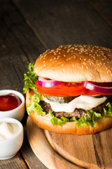 Close-up photo of home made hamburger with beer made of beef, onion, tomato, lettuce, cheese and spices. Fresh burger closeup on wooden rustic table with potato fries and chips.