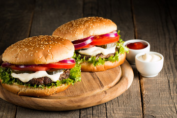 Close-up photo of home made hamburger with beer made of beef, onion, tomato, lettuce, cheese and spices. Fresh burger closeup on wooden rustic table with potato fries and chips.