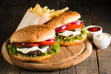 Close-up photo of home made hamburger with beer made of beef, onion, tomato, lettuce, cheese and spices. Fresh burger closeup on wooden rustic table with potato fries and chips.
