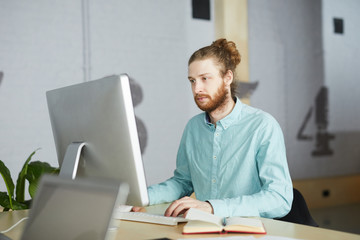 Fototapeta premium Portrait of bearded IT specialist using computer sitting at desk in office, copy space
