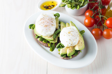 Avocado toast, cherry tomato on wooden background. Breakfast with toast avocado, vegetarian food, healthy diet concept. Healthy sandwich with avocado and poached eggs.