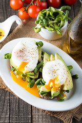 Avocado toast, cherry tomato on wooden background. Breakfast with toast avocado, vegetarian food, healthy diet concept. Healthy sandwich with avocado and poached eggs.
