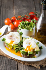 Avocado toast, cherry tomato on wooden background. Breakfast with toast avocado, vegetarian food, healthy diet concept. Healthy sandwich with avocado and poached eggs.