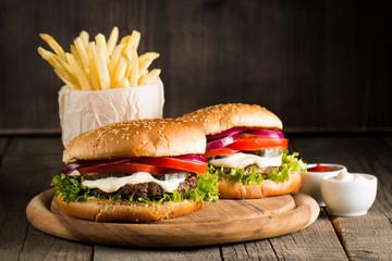 Close-up photo of home made hamburger with beer made of beef, onion, tomato, lettuce, cheese and spices. Fresh burger closeup on wooden rustic table with potato fries and chips.