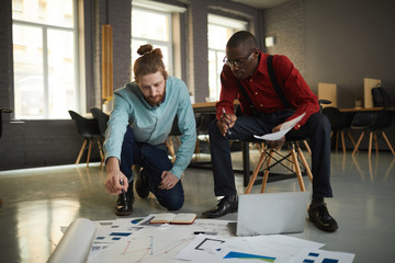 Full length portrait of two contemporary businessmen laying documents on floor while planning...