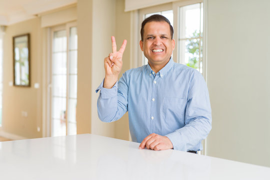 Middle age man sitting at home showing and pointing up with fingers number two while smiling confident and happy.