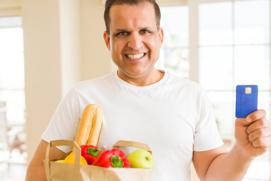 Middle age man holding groceries bag and showing credit card
