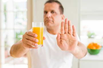 Fototapeta premium Middle age man drinking a glass of orange juice at home with open hand doing stop sign with serious and confident expression, defense gesture