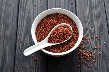 red rice in a ceramic bowl with spoon against dark wooden background